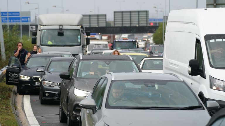 Drivers stand watching from their cars as traffic is halted during a roadblock by protesters from Insulate Britain at a roundabout leading from the M25 motorway to Heathrow Airport in London.