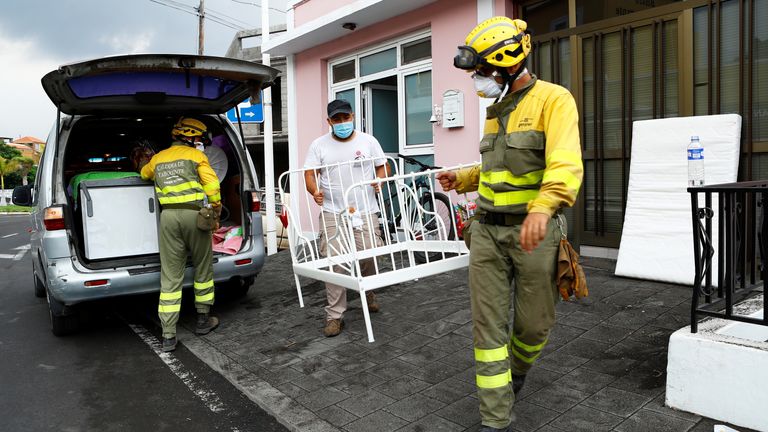 Members of the Forest Fire Reinforcement Brigades (BRIF) help a resident to carry furniture following the eruption of a volcano on the Canary Island of La Palma