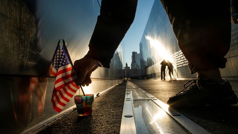A woman places a candle and a flag at the Empty Sky Memorial