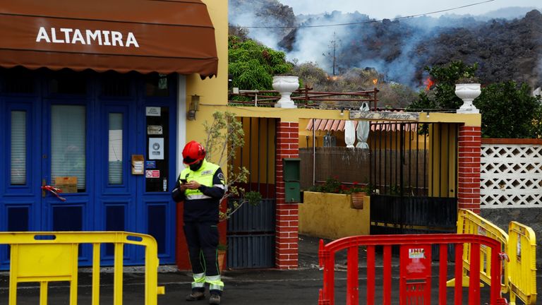 A member of emergency services stands by a building as lava from La Palma island volcano nears homes in Todoque, Spain