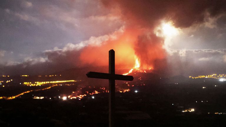 A cross is seen as lava and smoke rise following the eruption of a volcano on the Island of La Palma, in Los Llanos de Aridane, Spain September 21, 2021. Picture taken September 21, 2021. REUTERS/Nacho Doce
