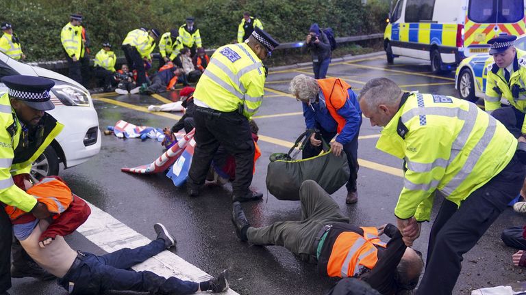 Police officers detain a protester from Insulate Britain occupying a roundabout leading from the M25 motorway to Heathrow Airport in London.  