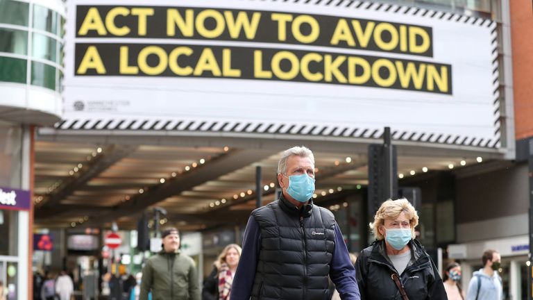People wearing face masks walk past a advertisement on Market Street in Manchester, as the city is waiting to find out if the region will be placed into the Very High category with tier 3 lockdown restrictions to curb the spread of coronavirus.