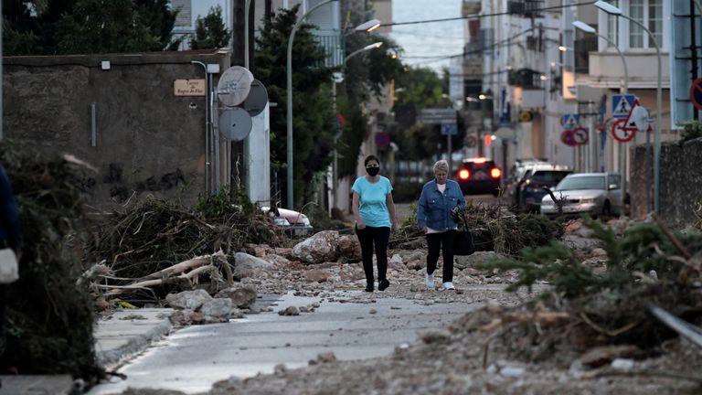 Wanita berjalan di jalan yang terhalang oleh pohon tumbang dan batu setelah banjir yang disebabkan oleh hujan lebat di Alcanar, Spanyol 