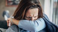 One woman, young woman with Covid-19 symptoms sitting on sofa at home, holding thermometer.