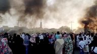 People gather on the streets as smoke rises in Khartoum,  Sudan, amid reports of a coup, 