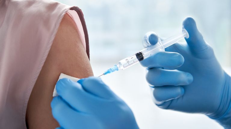 Male doctor holding syringe making covid 19 vaccination injection dose in shoulder of female patient wearing mask. Flu influenza vaccine clinical trials concept, corona virus treatment, close up view.