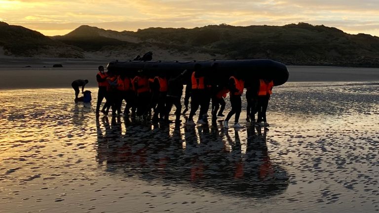 Migrants  - manhandling a large inflatable boat down a northern French beach, to get to the seafront in order to to cross the Channel.  - re copy from  Adam Parsons and Sophie Garratt