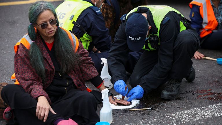 A police officer tries to remove the hand of a demonstrator glued to the road as Insulate Britain activists block a roundabout at a junction on the M25 motorway as they a protest in Thurrock, Britain October 13, 2021. REUTERS/Henry Nicholls
