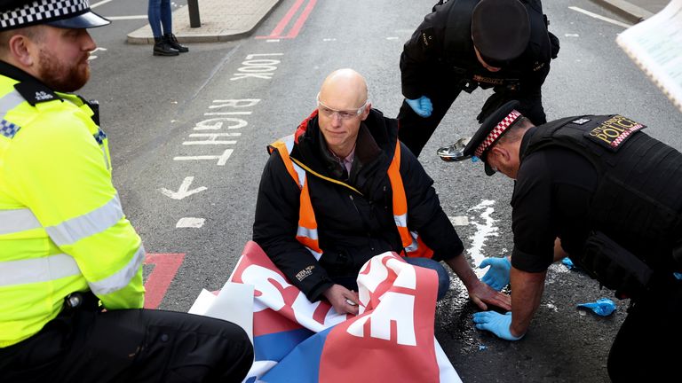 A police officer tries to remove the hand of an Insulate Britain activist glued to the road, during a protest in London, Britain October 25, 2021. REUTERS/Henry Nicholls
