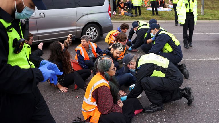 Police officers try to remove hands of Insulate Britain activists glued to the ground as they block a roundabout at a junction on the M25 motorway during a protest in Thurrock, Britain October 13, 2021. REUTERS/Henry Nicholls
