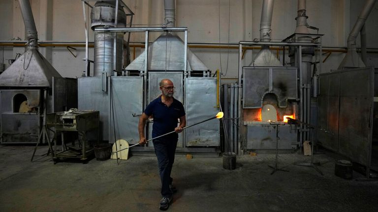 A glass-worker works at a glass artistic creation as he walks past methane powered ovens in a factory in Murano island, Venice. Pic: AP