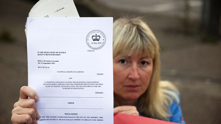 A demonstrator shows an High Court injunction paper as Insulate Britain activists block a roundabout at a junction on the M25 motorway during a protest in Thurrock, Britain October 13, 2021. REUTERS/Henry Nicholls
