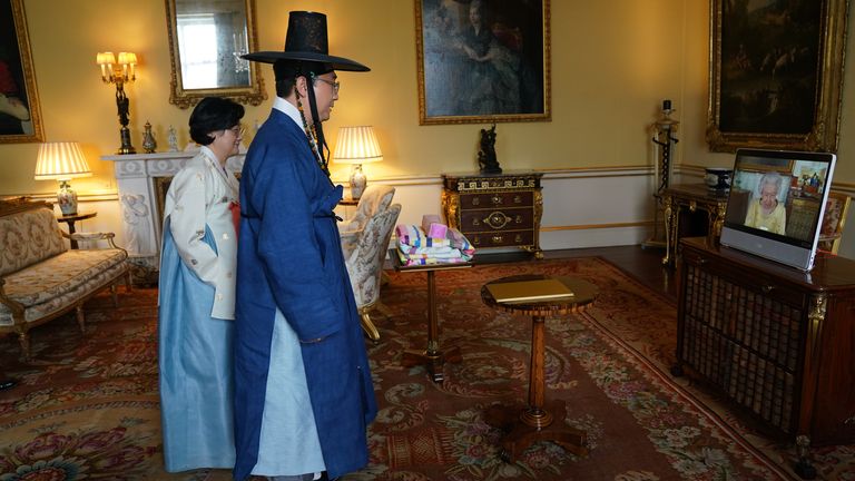 Królowa Elżbieta II pojawia się na ekranie za pośrednictwem łącza wideo z zamku Windsor, gdzie przebywa, podczas wirtualnej audiencji, aby powitać ambasadora Republiki Korei, Johna Kima, w towarzystwie Hyejong Lee (z lewej), w Pałacu Buckingham w Londynie.  Data zdjęcia: wtorek, 26 października 2021 r.