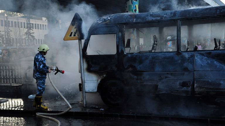 In this photo released by the Syrian official news agency SANA, shows a Syrian firefighter extinguishes a burned bus at the site of a deadly explosion, in Damascus, Syria, Wednesday, Oct. 20, 2021. Two roadside bombs exploded near a bus carrying troops during the morning rush hour in the Syrian capital early Wednesday, killing and wounding several people, state TV reported.(SANA via AP)