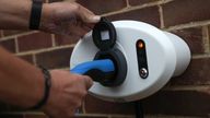 A person places an electric charging cable into BP Chargemaster electric vehicle charging point at a residential home.
