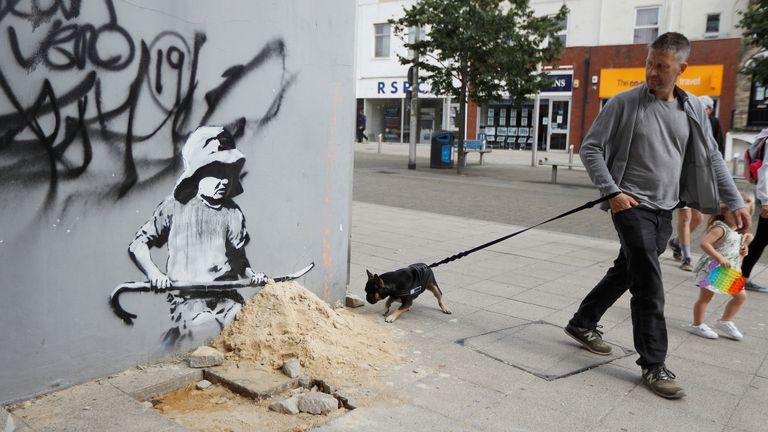 A man and his dog walk past artwork created by Banksy in Lowestoft, Britain, August 8, 2021. REUTERS/Peter Nicholls