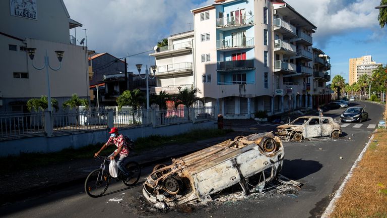 A man rides his bicycle past burned cars after violent demonstrations which broke out over coronavirus disease (COVID-19) protocols