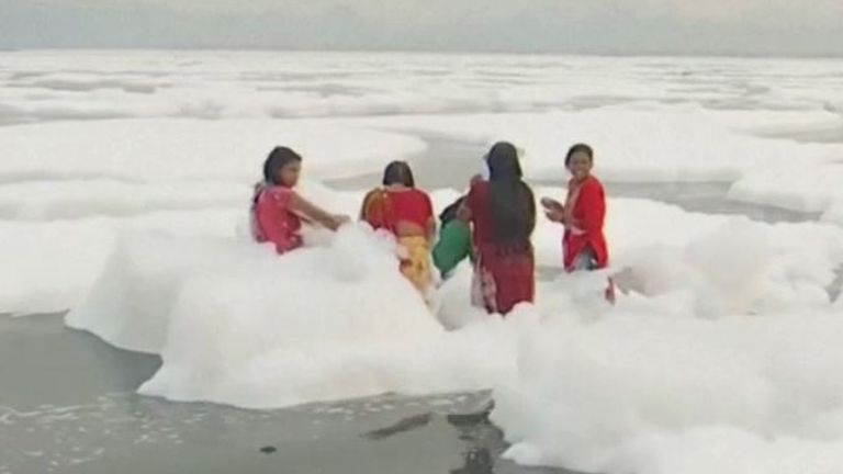 Hindu women bathe in the Yamuna River, despite it being covered in toxic foam