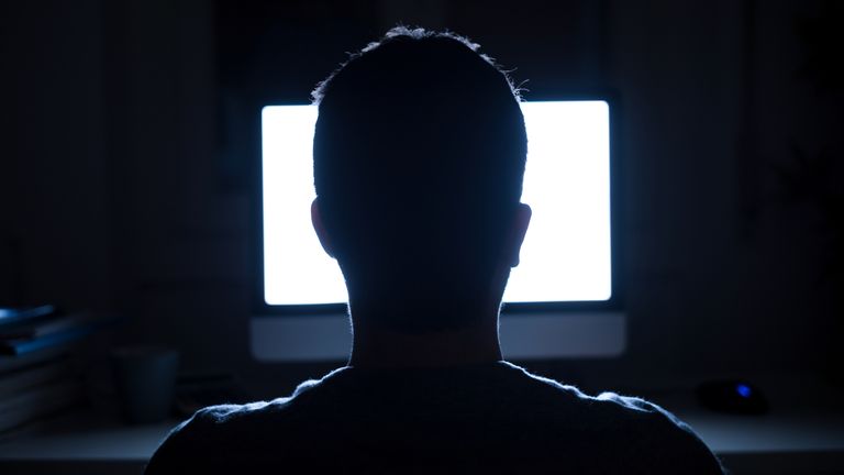 Silhouette of man's head in front of computer monitor light at night