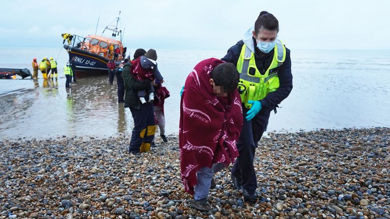 یک افسر گارد مرزی در حالی که گروهی از مردم که گمان می‌رود مهاجر هستند توسط RNLI پس از یک حادثه قایق کوچک در کانال انگلیسی در 20 نوامبر به دانگنز، کنت آورده شدند، به پسری کمک کرد.