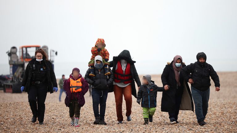 Migrants walk along a beach as they are escorted by a police officer after being brought ashore by a RNLI Lifeboat, after having crossed the channel, in Dungeness, Britain, November 24, 2021. REUTERS/Henry Nicholls
