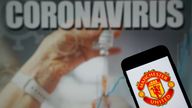 The Manchester United Football Club logo seen displayed on a mobile phone with a COVID illustration on a monitor in the background