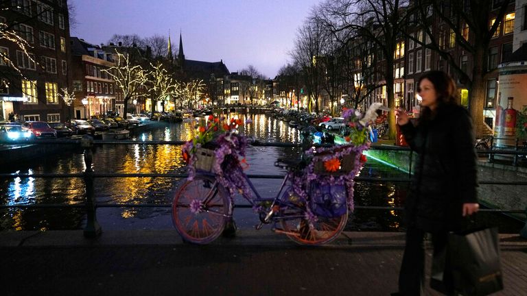A woman crosses a canal in Amsterdam, the Netherlands on Saturday, Dec. 18, 2021.  Dutch government ministers are meeting Saturday to discuss advice from a panel of experts who are reportedly are advising a toughening of the partial lockdown that is already in place to combat COVID-19. (AP Photo/Peter Dejong)