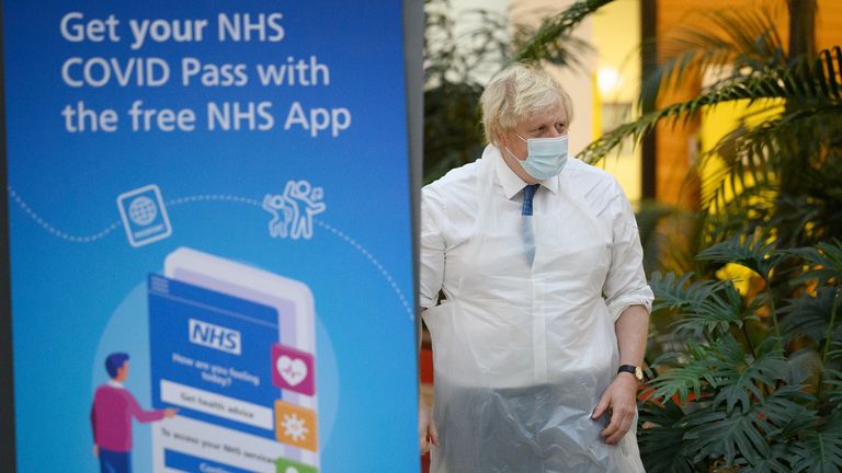 Prime Minister Boris Johnson walks past a poster advertising the NHS COVID Pass during a visit to a vaccination centre in Ramsgate, Kent. Picture date: Thursday December 16, 2021.
