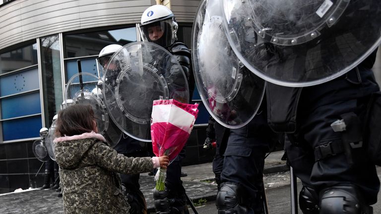 A girl gives flowers to riot police officers during a protest against coronavirus measures in Brussels, Belgium, Sunday, Dec. 5, 2021. Hundreds of people marched through central Brussels on Sunday to protest tightened COVID-19 restrictions imposed by the Belgian government to counter the latest spike in coronavirus cases. (AP Photo/Geert Vanden Wijngaert)