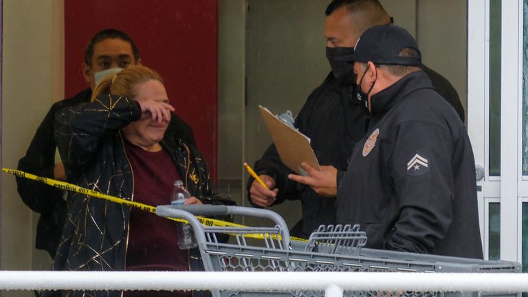 A woman wipes her eye as police officers investigate the scene where two people were struck by gunfire. Pic: AP