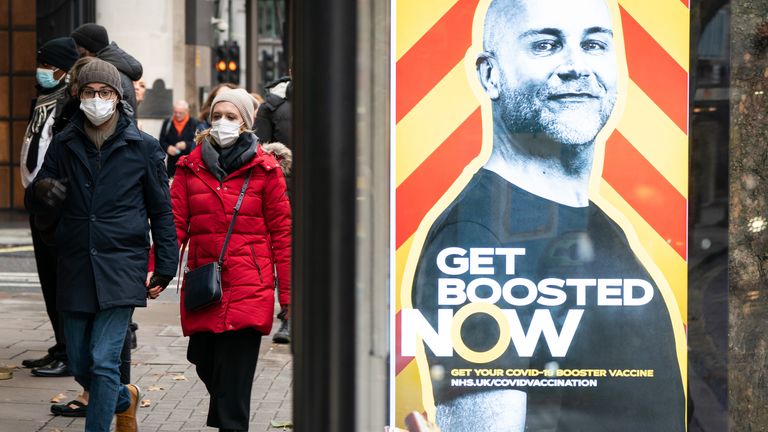 People wearing face masks walk past a UK government ad urging people to order covid-booster vaccinations in central London.  It has been announced that no further coronavirus restrictions will be introduced in the UK before the New Year.  Image Date: Tuesday, December 28, 2021.