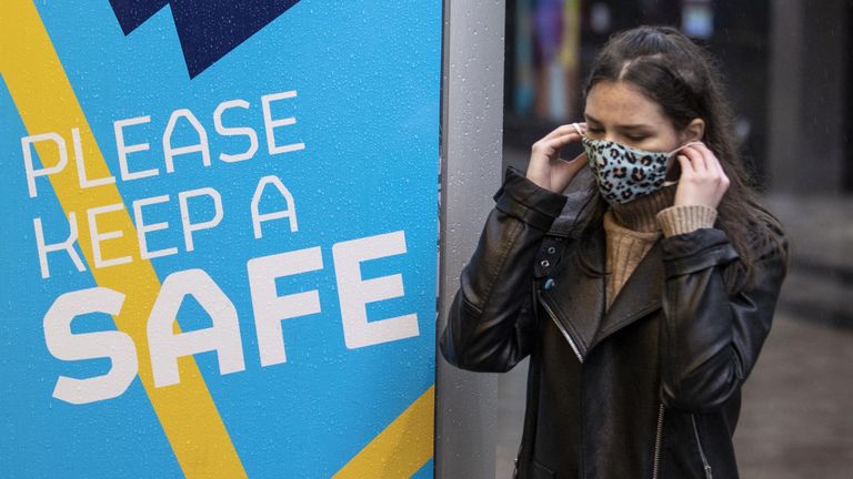 A young woman in Belfast puts on her face covering as she walks past a Covid-19 safety message from Belfast City Council.