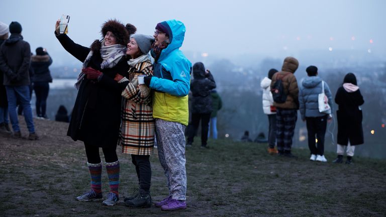 مردم در سپیده دم در اولین روز سال 2021 در تپه پامچال در برابر پس‌زمینه اپیدمی بیماری کروناویروس (COVID-19) در لندن، بریتانیا، 1 ژانویه 2021 سلفی می‌گیرند. رویترز / جان سیبلی