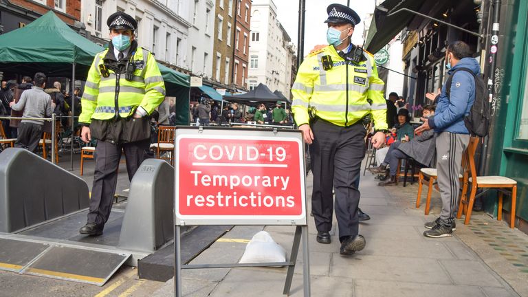 London, United Kingdom - 12th April 2021: Police officers walk past a Covid-19 Temporary Restrictions sign in Old Compton Street, Soho. Several streets in Central London have been blocked for traffic at certain times of the day to allow outdoor, al fresco seating for bars and restaurants during the coronavirus pandemic.
