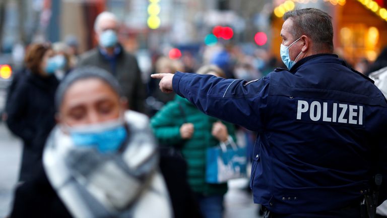 A police officer checks if people are wearing masks in a main shopping area of Cologne, Germany