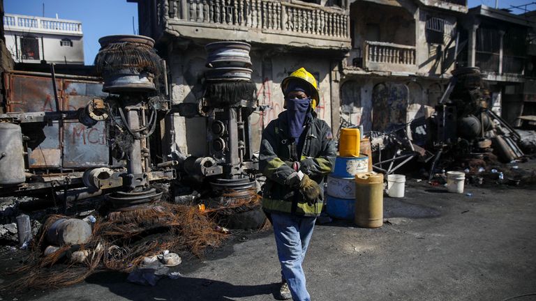 A firefighter stands next to the remains of a truck that was carrying gasoline and overturned in Cap-Hatien, Haiti, Tuesday, Dec. 14, 2021. The truck exploded, engulfing cars and homes in flames, killing more than 50 people and injuring dozens of others. (AP Photo/Joseph Odelyn)


