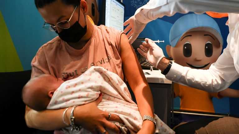 زنی هنگام دریافت سومین نوبت واکسن کووید-19 در اورشلیم نوزاد خود را تاب می دهد. 
