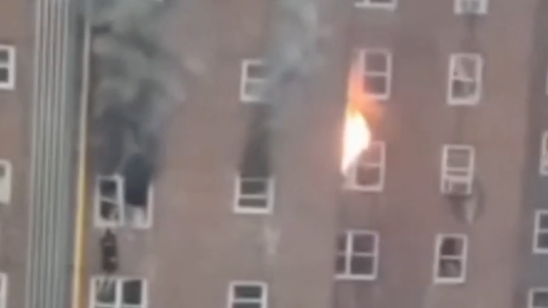 یکی را می توان در حال بالا رفتن از پنجره دید که شعله های آتش و دود سیاه نیز از ساختمان بلند می شود.