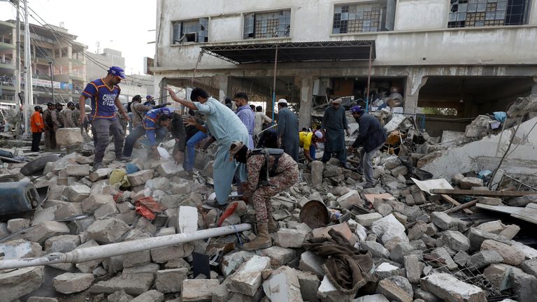 People and paramilitary personnel clear the rubble after a blast in an industrial area in Karachi