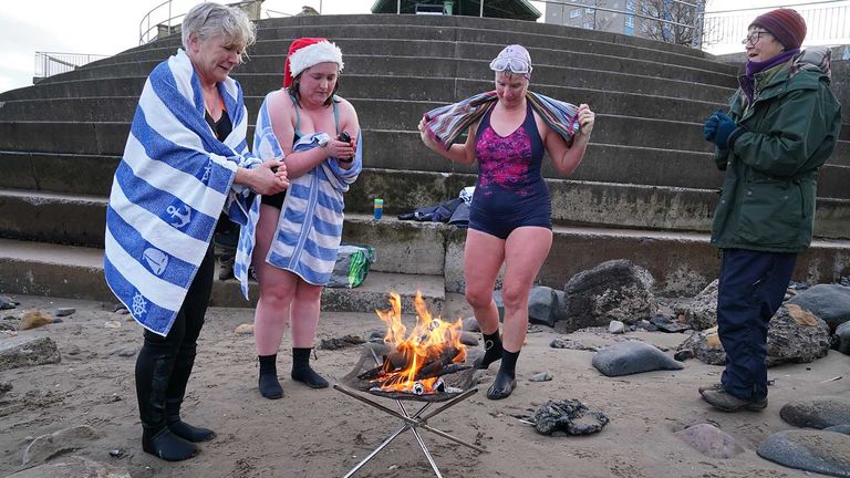 Wild swimmers dry off by a fire after taking a Christmas Day dip at Portobello Beach in Edinburgh. Picture date: Saturday December 25, 2021.