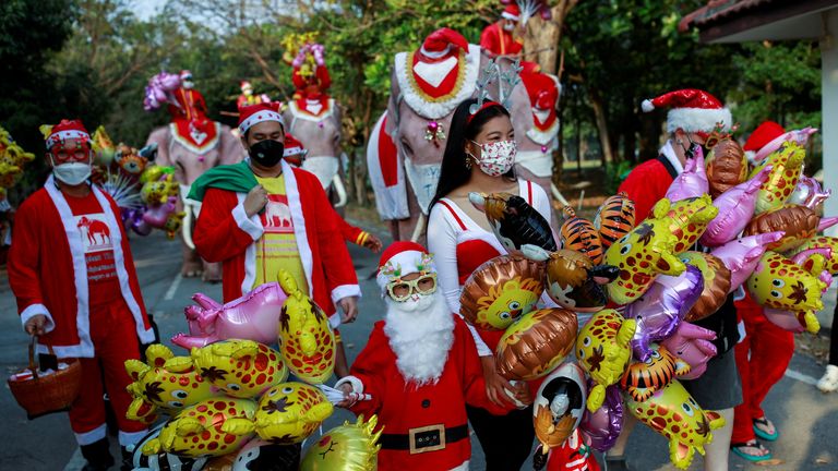 People in Santa Claus costumes walk during the visit of five elephants wearing Santa Claus costumes with giant face masks, delivering hand sanitizers and promoting a &#34;get vaccinated&#34; message to a primary school in the historical city of Ayutthaya, Thailand, December 24, 2021. REUTERS/Soe Zeya Tun