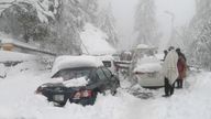 Cars stuck under fallen trees on a snowy road, in Murree