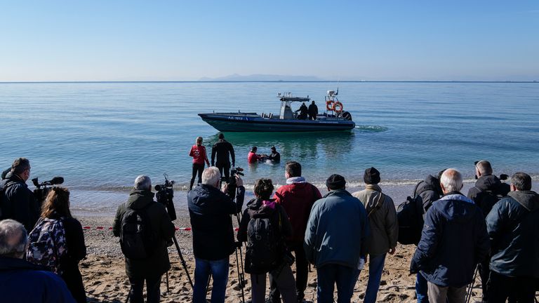 گروه‌های تلویزیونی پشت نوار ایستاده‌اند در حالی که تیم‌های نجات متشکل از غواصان و دامپزشکان تلاش می‌کنند از یک گوساله نهنگ که در آب‌های کم عمق در منطقه ساحلی جنوب آتن در روز جمعه، 28 ژانویه 2022 به گل نشسته، مراقبت کنند. کارشناسان می‌گویند این حیوان جوان یک کوویر است. منقار نهنگ و اینکه او نشانه هایی از جراحت داشت.  (عکس AP/ تاناسیس استاوراکیس) PIC: AP