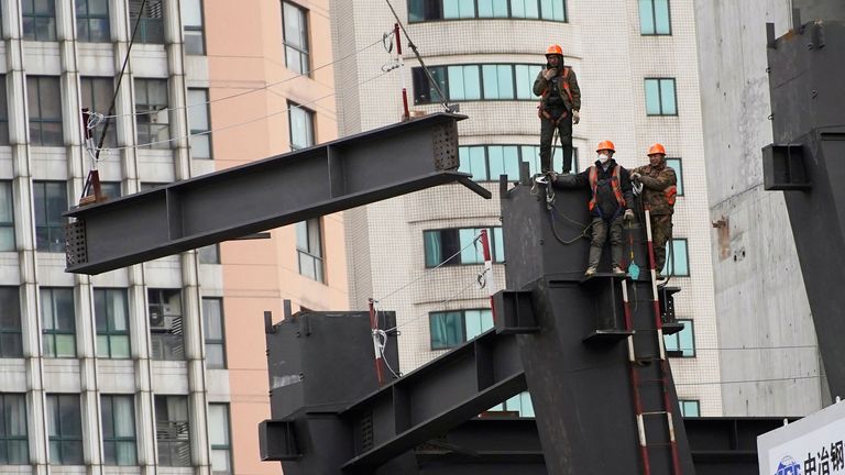 Des travailleurs regardent une grue soulever une structure sur un chantier de construction à Shanghai, en Chine, le 14 janvier 2022