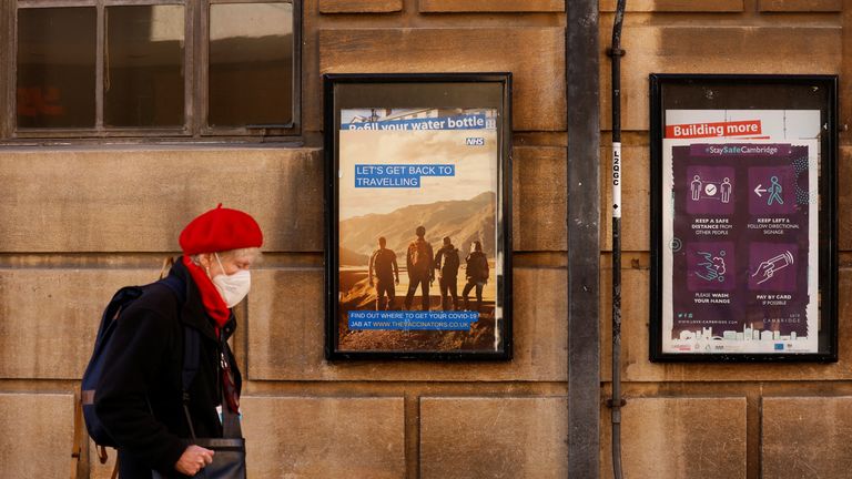A woman wearing a face mask walks past posters in Cambridge highlighting messages to stay safe, amid the coronavirus pandemic