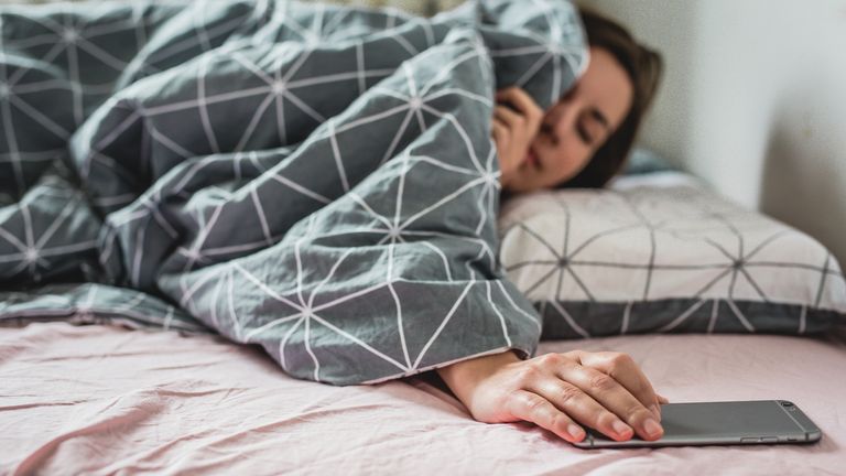 A young woman wakes up the bed. the alarm on the smartphone is ringing Pic from iStock