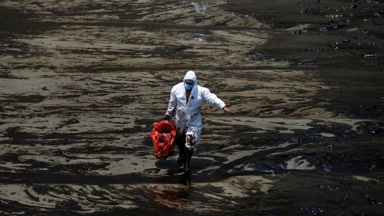 A worker walks following an oil spill caused by abnormal waves, triggered by a massive underwater volcanic eruption half a world away in Tonga, at the Peruvian beach in Ventanilla, Peru, 18 January 2022. REUTERS/Pilar Olivares