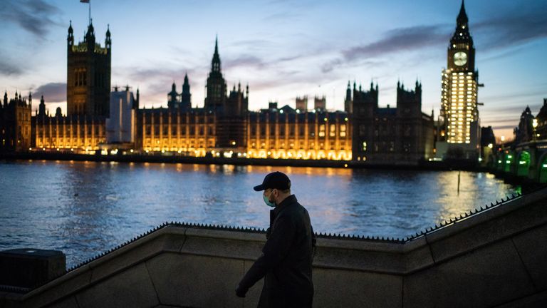زنی در شب از مقابل ساختمان پارلمان در وست مینستر لندن عبور می کند، زمانی که بریتانیا بیش از 200000 مورد ابتلا به ویروس کرونا را در یک روز برای اولین بار ثبت کرد تاریخ: سه شنبه، 4 ژانویه 2022