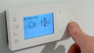 A homeowner turns down the temperature of a central heating thermostat